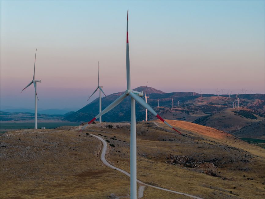 A scenic view of wind turbines on rolling hills at sunset, showcasing renewable energy.