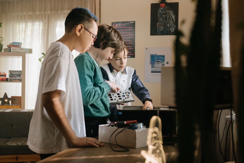 Three young teens work together on a computer project indoors, exploring hardware and technology.