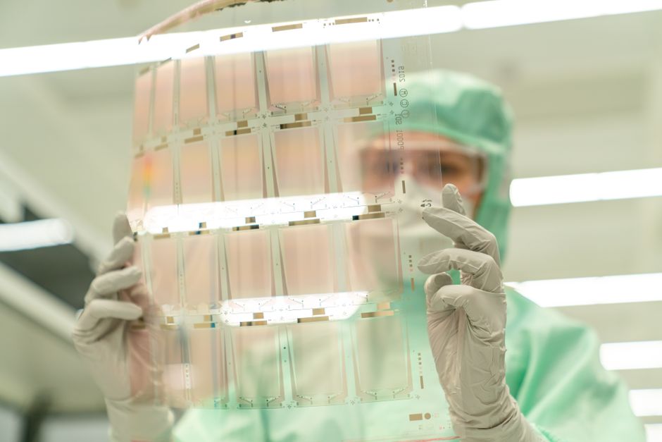 Scientist in protective gear holding a transparent test sheet in a laboratory.