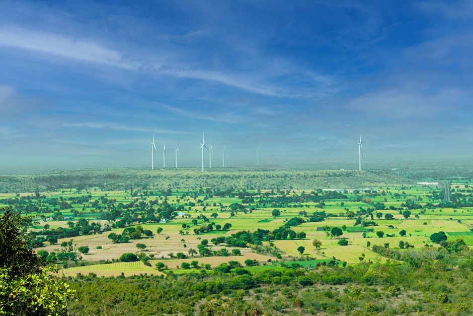 A stunning view of wind turbines towering over vibrant green fields under a clear blue sky in Rajapur, India.