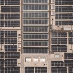 A high-angle drone shot capturing a grid of solar panels on a large industrial rooftop, showcasing renewable energy.