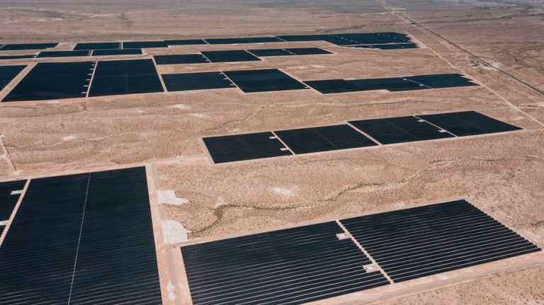 Drone shot of a large solar farm in a desert landscape, showcasing renewable energy infrastructure.