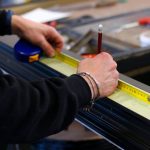A worker measuring aluminum with a tape measure in a workshop, showcasing precision and craftsmanship.