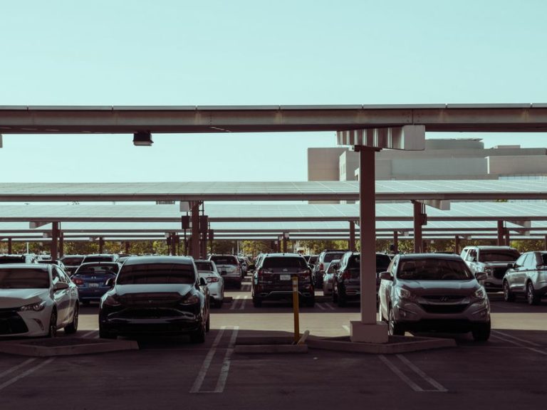 A modern parking lot with cars under solar panel structures for sustainable energy use.