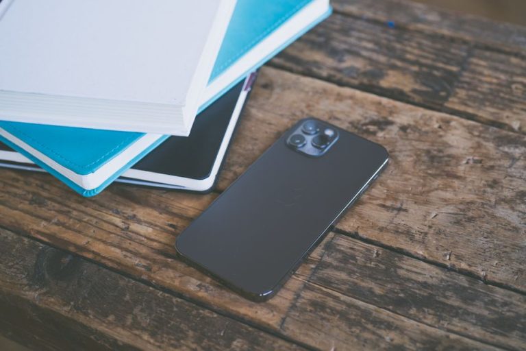 A modern smartphone placed beside assorted notebooks on a rustic wooden surface