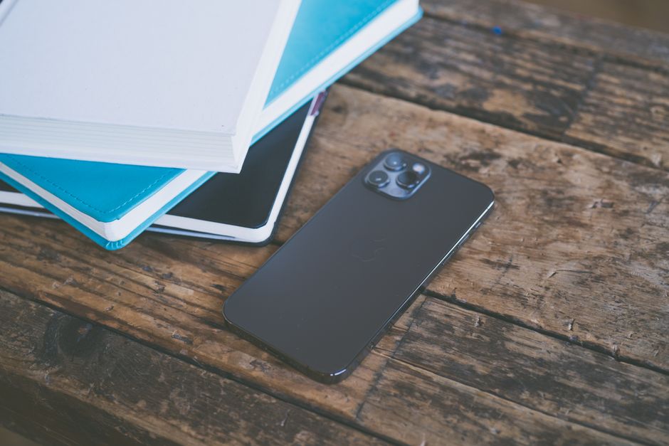 A modern smartphone placed beside assorted notebooks on a rustic wooden surface