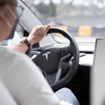 Close-up photo of a person driving a Tesla, showcasing modern vehicle interior design.
