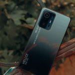 A close-up of a smartphone placed outdoors with a nature background, showcasing design details.
