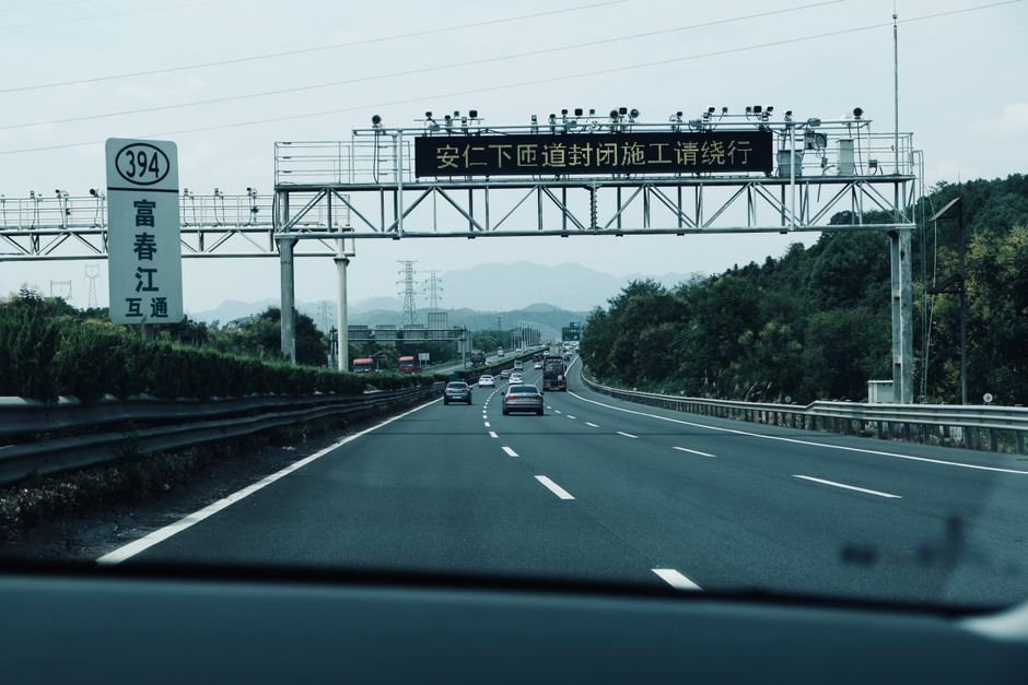 A busy highway in Asia with traffic signs and cars on a cloudy day.