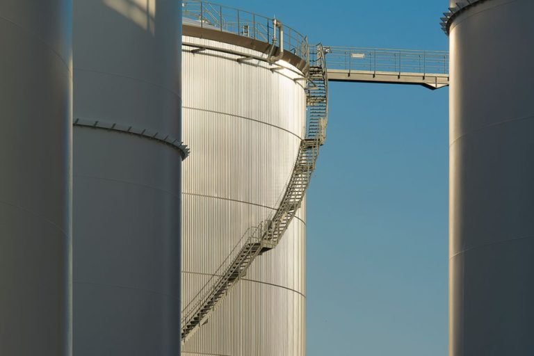Close-up view of metal industrial silos with a connecting staircase against a clear blue sky.