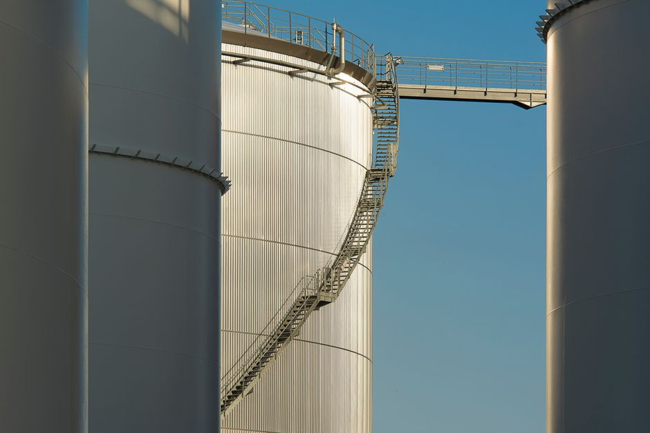Close-up view of metal industrial silos with a connecting staircase against a clear blue sky.
