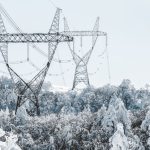 A scenic view of transmission towers amidst snow-covered trees during winter.