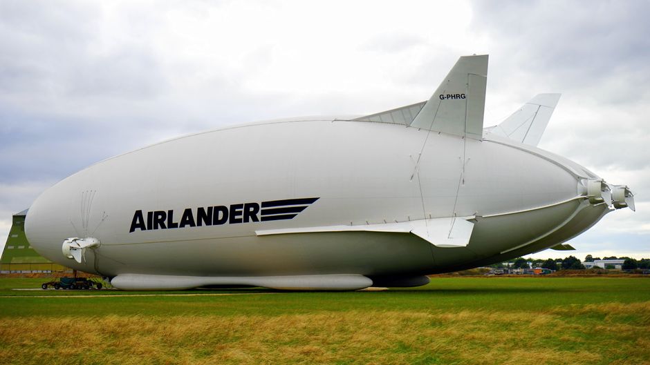 A large Airlander hybrid airship parked on a grassy field under a cloudy sky.
