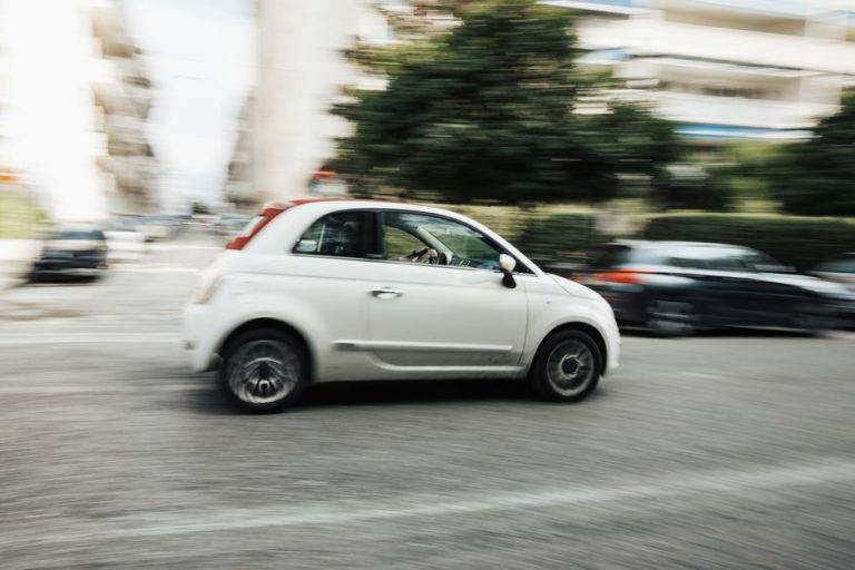 White car speeding through city street with motion blur effect highlighting fast motion.