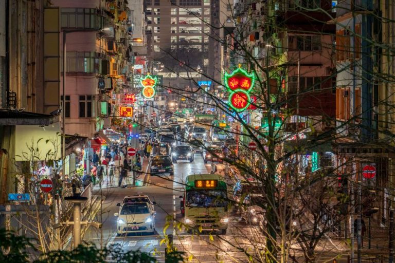 Vibrant city street illuminated by neon lights, buzzing with nighttime traffic and activity.