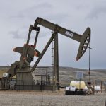 Oil pump jack and equipment at remote industrial site under cloudy sky.