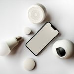 Flat lay of smartphone and smart home devices on a white backdrop, showcasing modern technology.