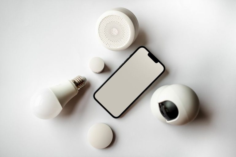 Flat lay of smartphone and smart home devices on a white backdrop, showcasing modern technology.