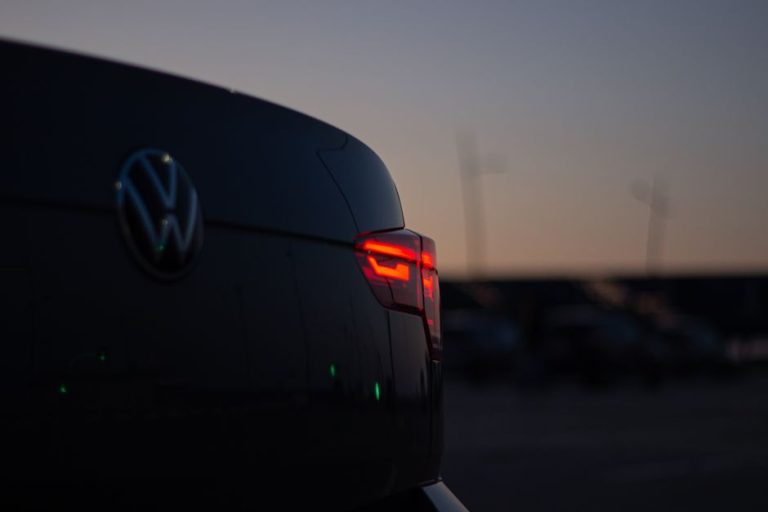 A close-up of a car's taillight glowing red against the evening sky.
