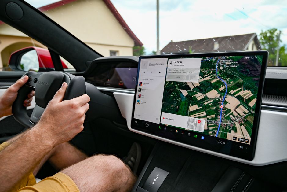 Man driving Tesla using GPS on touchscreen dashboard for navigation.