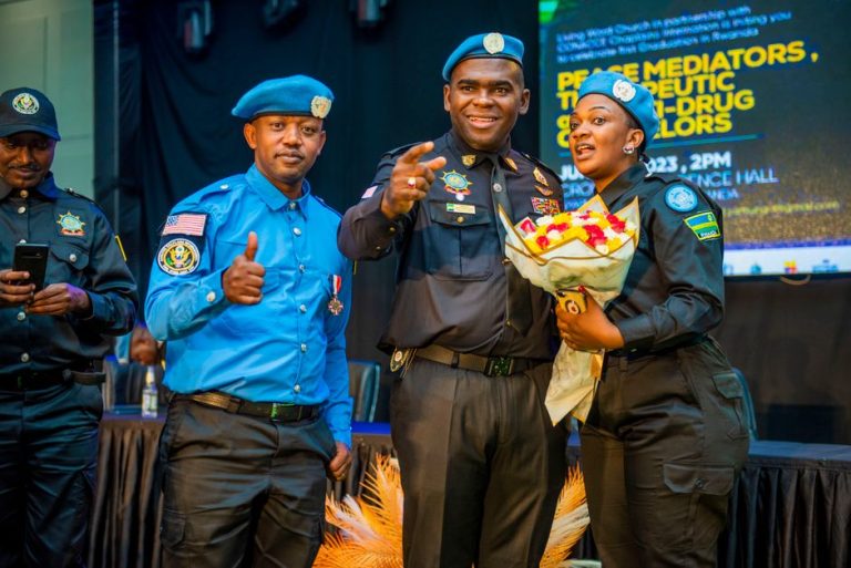 Group of police officers posing indoors, one holding a bouquet, wearing uniforms.
