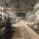 Spacious industrial warehouse interior featuring machinery and network of pipes.