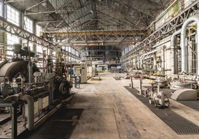 Spacious industrial warehouse interior featuring machinery and network of pipes.