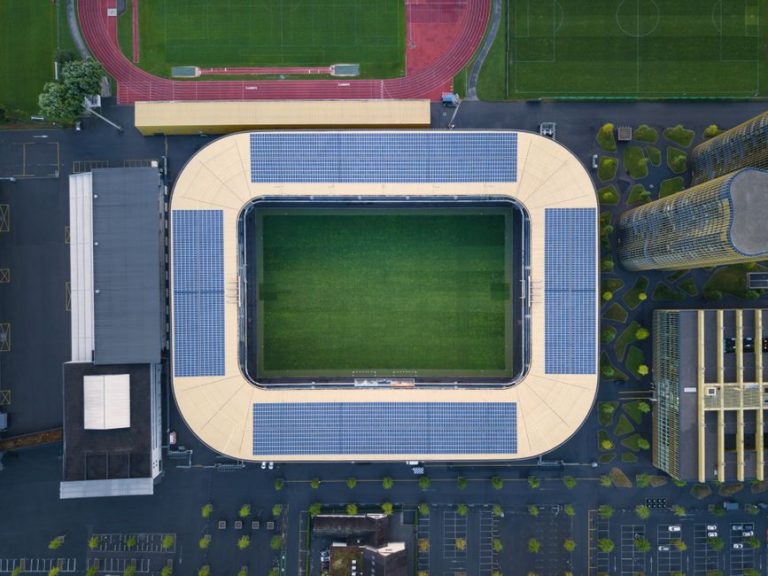 Drone shot of a modern stadium with solar panels and sports fields.