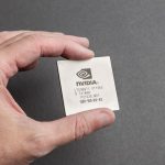 A close-up view of a person holding an Nvidia chip with a gray background.