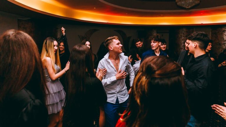 A lively group of teenagers dancing indoors at a party with vibrant lighting and joyous expressions.