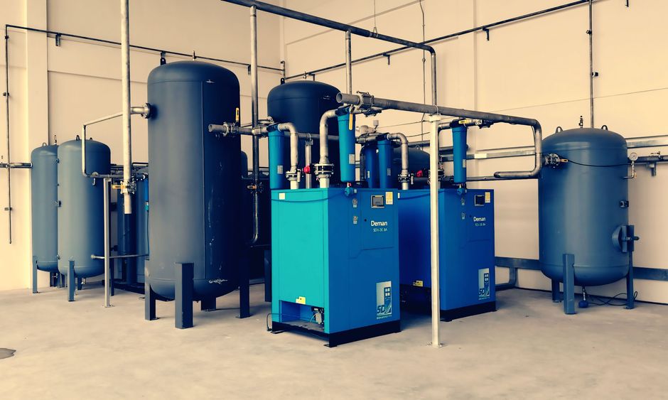 Industrial air compressor setup with blue tanks and pipes inside a plant.