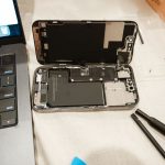 Open iPhone with repair tools and laptop, showcasing DIY battery replacement process.