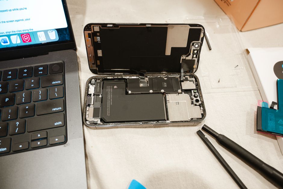 Open iPhone with repair tools and laptop, showcasing DIY battery replacement process.