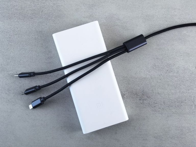 A sleek white power bank with a black multi-connector cable laid on a textured grey surface, emphasizing modern technology.