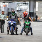 Motorcyclists in helmets at a border checkpoint interacting with a police officer outdoors.