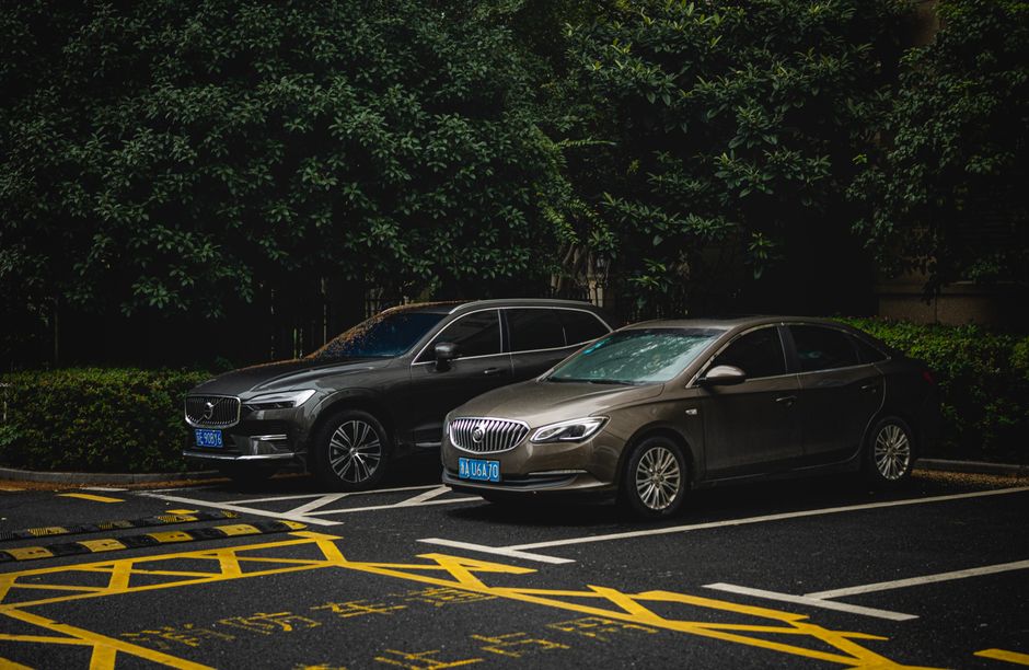 Two cars, an SUV and a sedan, parked side by side in a shady urban lot.