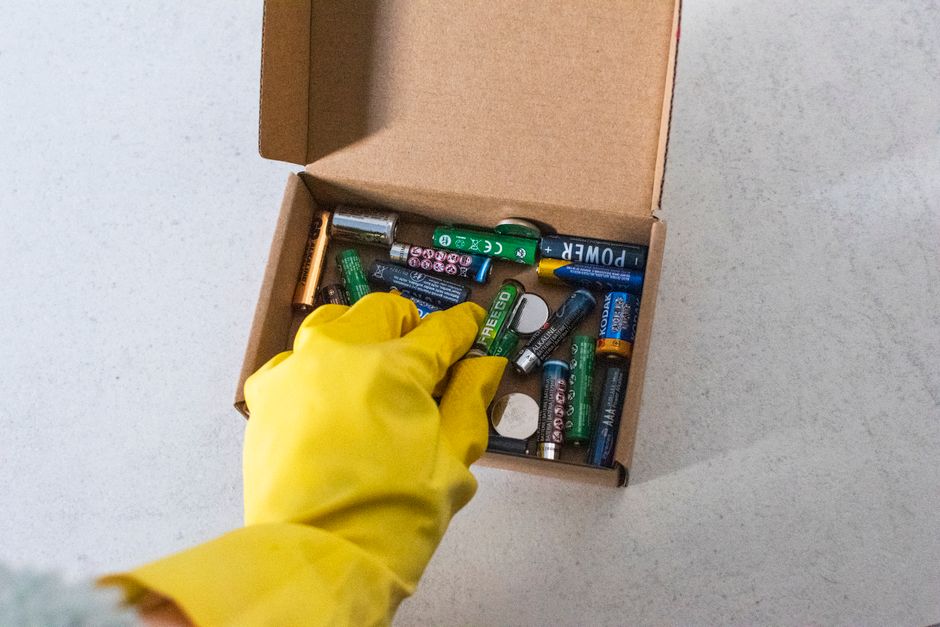 Yellow-gloved hand handling used batteries for safe recycling.