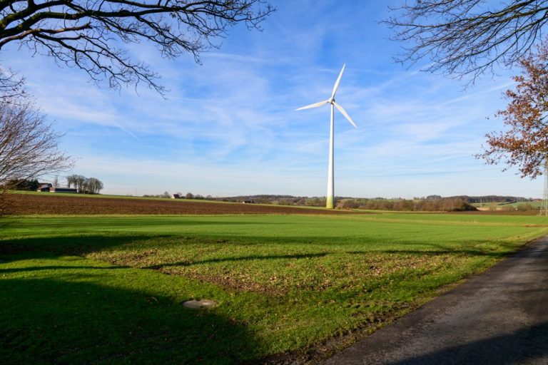 A wind turbine stands tall in a vast green field under a blue sky in Coesfeld, Germany.