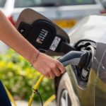 Close-up of a person plugging in an electric car at a charging station outdoors.