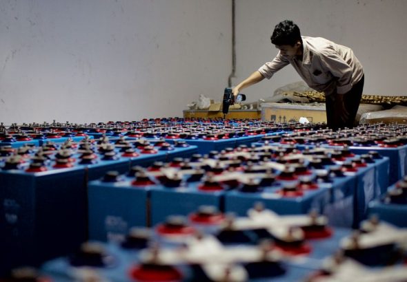 A worker checking many industrial batteries inside a facility. Indoor, industrial setting.