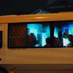 Silhouetted passengers on a bus at night with city lights reflecting on the windows.