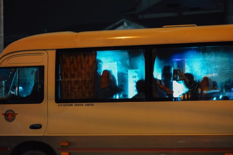 Silhouetted passengers on a bus at night with city lights reflecting on the windows.