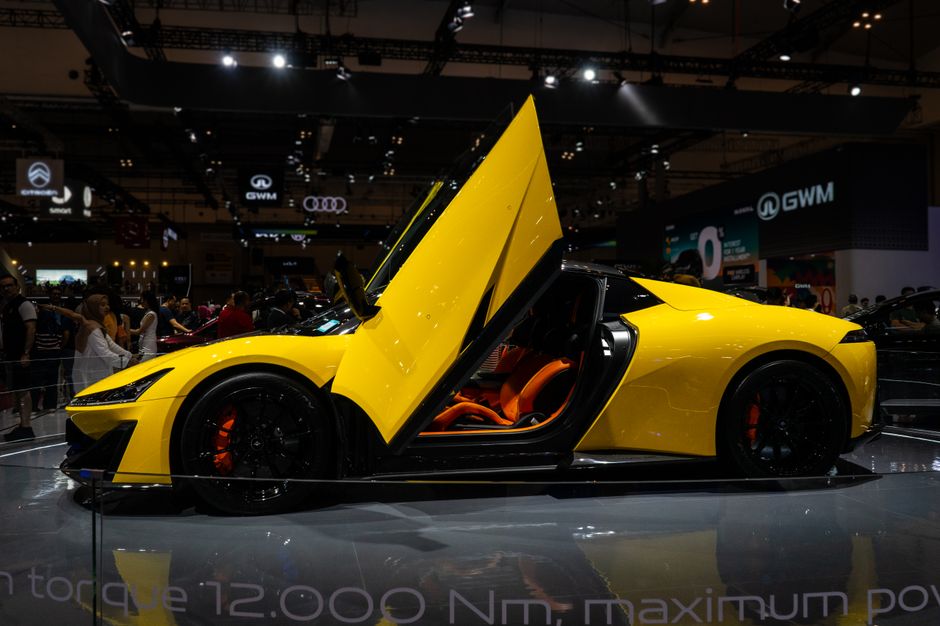 A sleek yellow sports car with butterfly doors showcased at an auto exhibition.