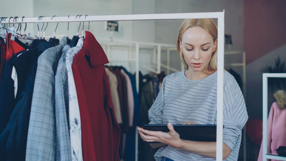 Female retail employee using a tablet for inventory management in a clothing store.