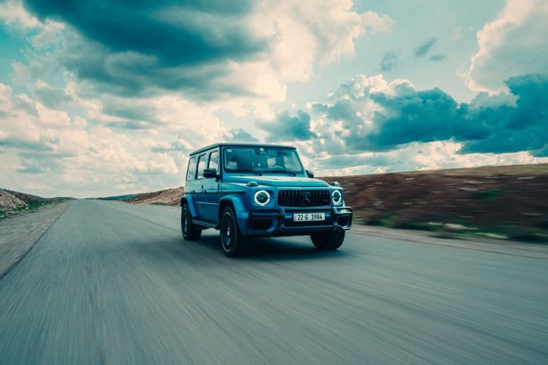 Mercedes-Benz G-Class SUV driving fast down an open road under dramatic clouds.