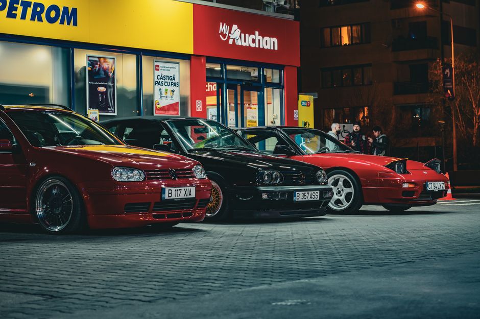Three vintage cars parked at a gas station at night, showcasing classic automotive design.