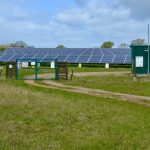 Large solar power station with panels in an open green field under a cloudy sky.