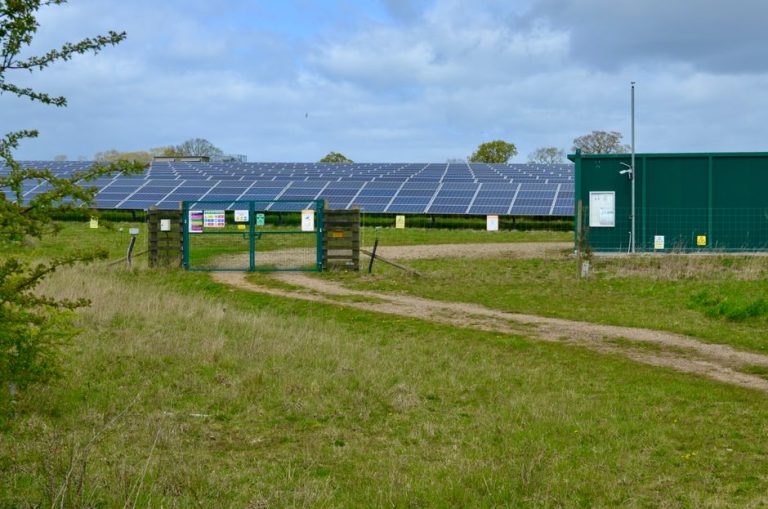 Large solar power station with panels in an open green field under a cloudy sky.