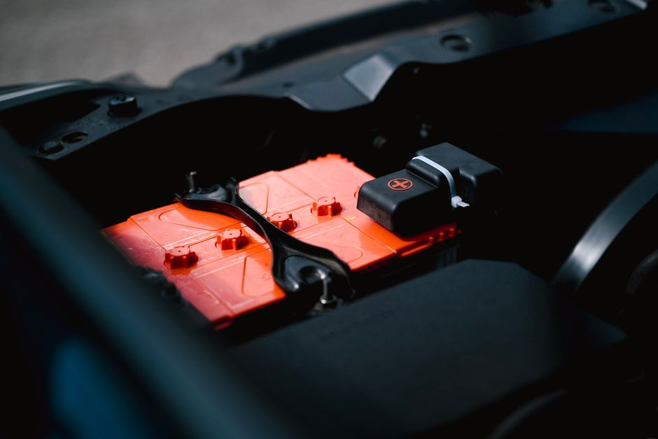 Detailed view of an orange car battery inside a vehicle's engine bay, highlighting its features.