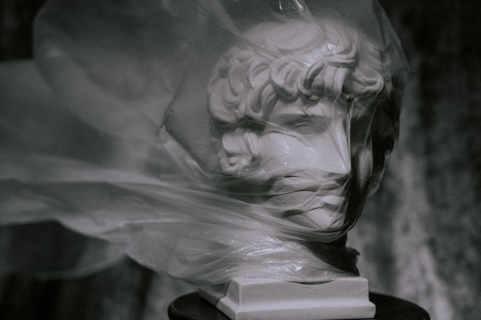 Statue covered with plastic highlighting environmental concerns.